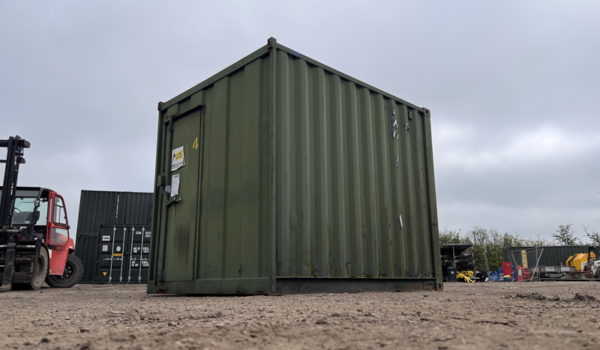 Ground-level view of green 8ft storage container on gravel surface with cloudy sky